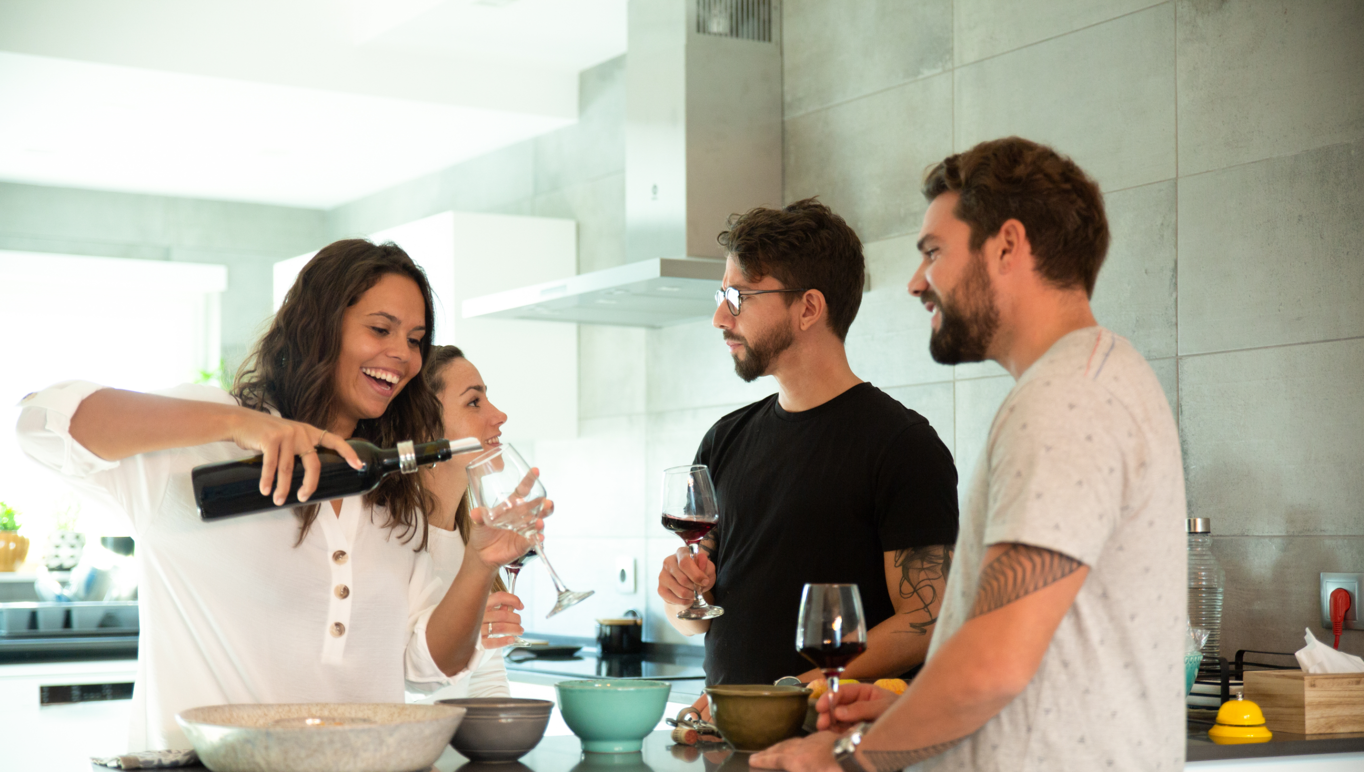 Dos parejas tom&aacute;ndose un vino dentro de la cocina relajados y ri&eacute;ndose 