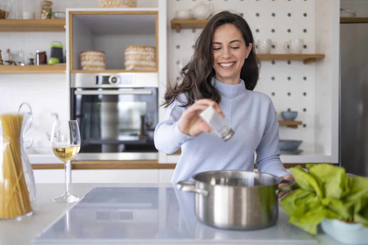 Una mujer feliz cocinando ech&aacute;ndole sal a una cacerola