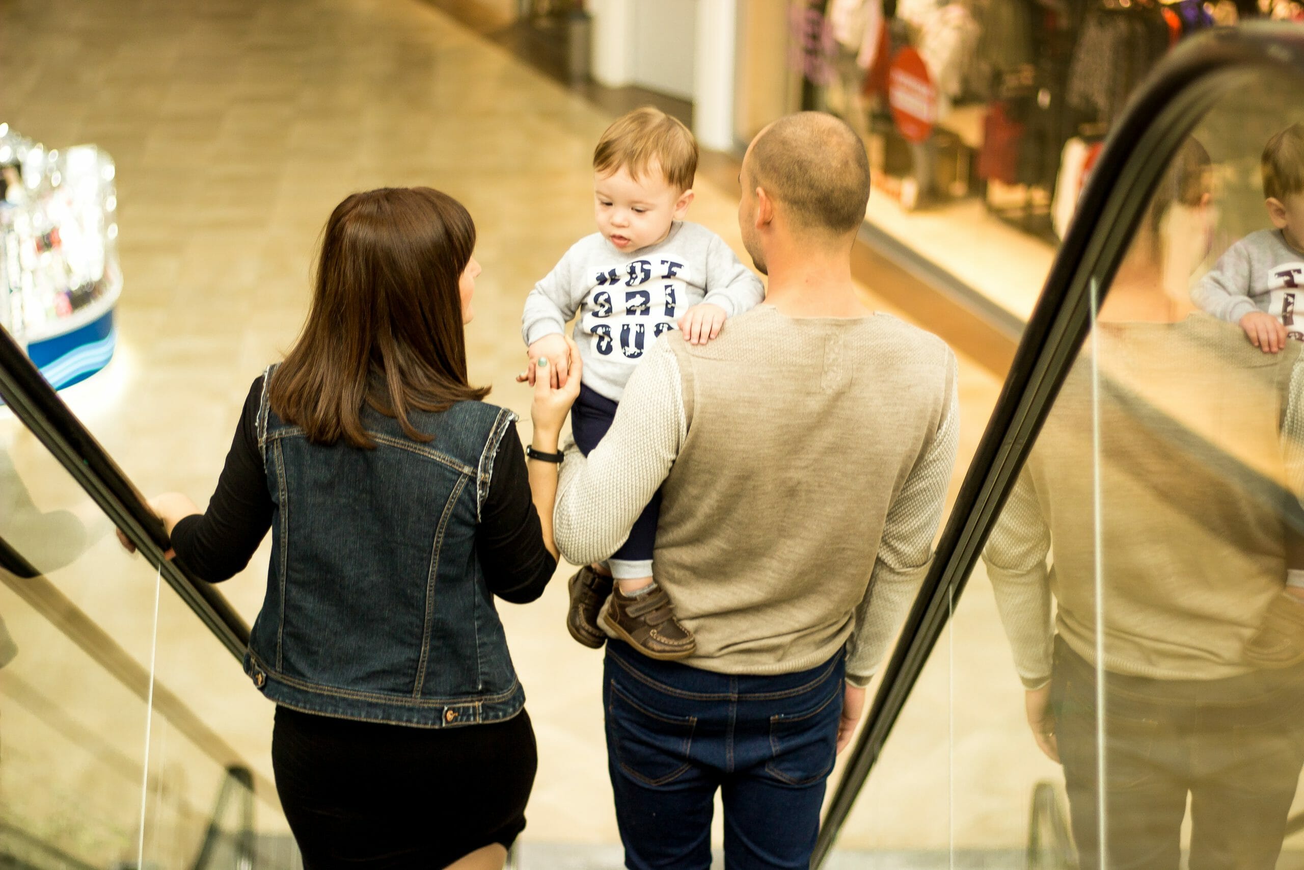 Familia bajando por una escalera el&eacute;ctrica de un centro comercial mientras est&aacute;n de compras