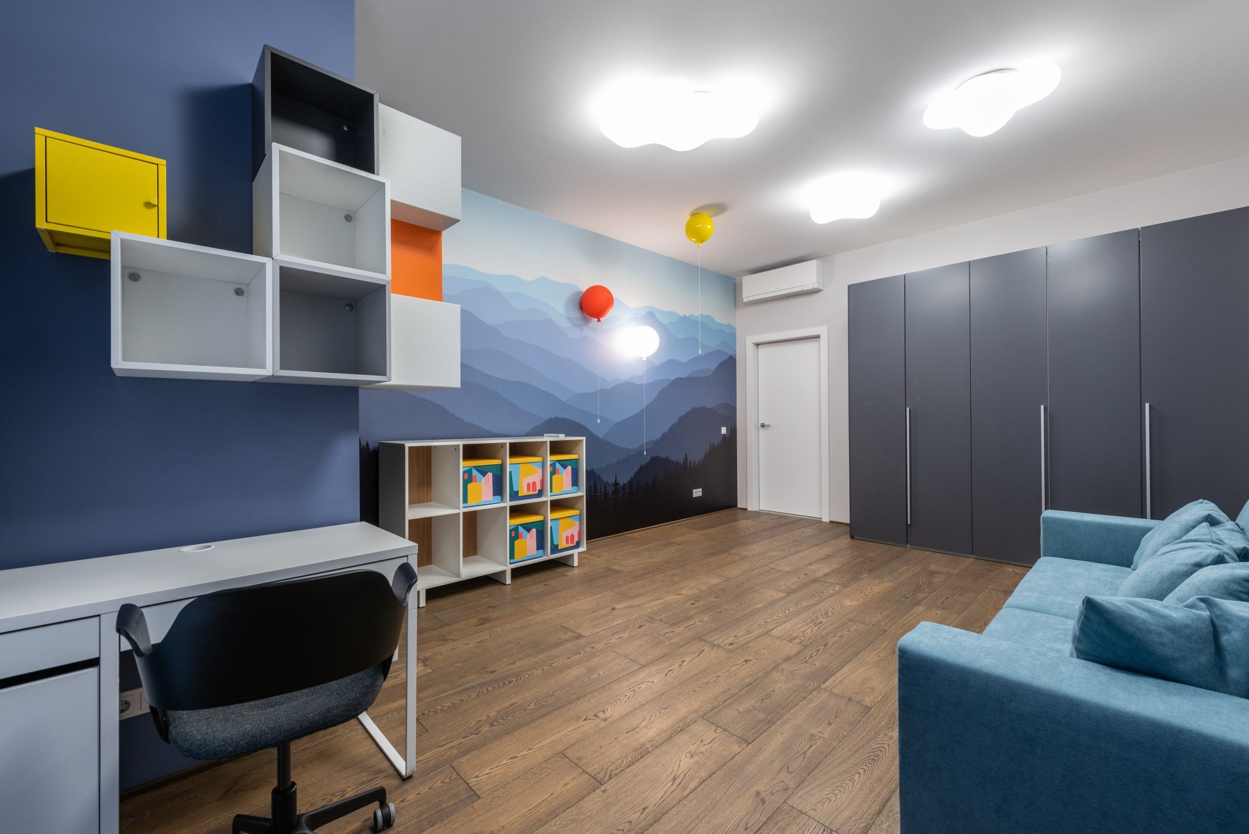 Habitaci&oacute;n decorada con estantes, sof&aacute; y escritorio, y un papel tapiz en tonos azules.