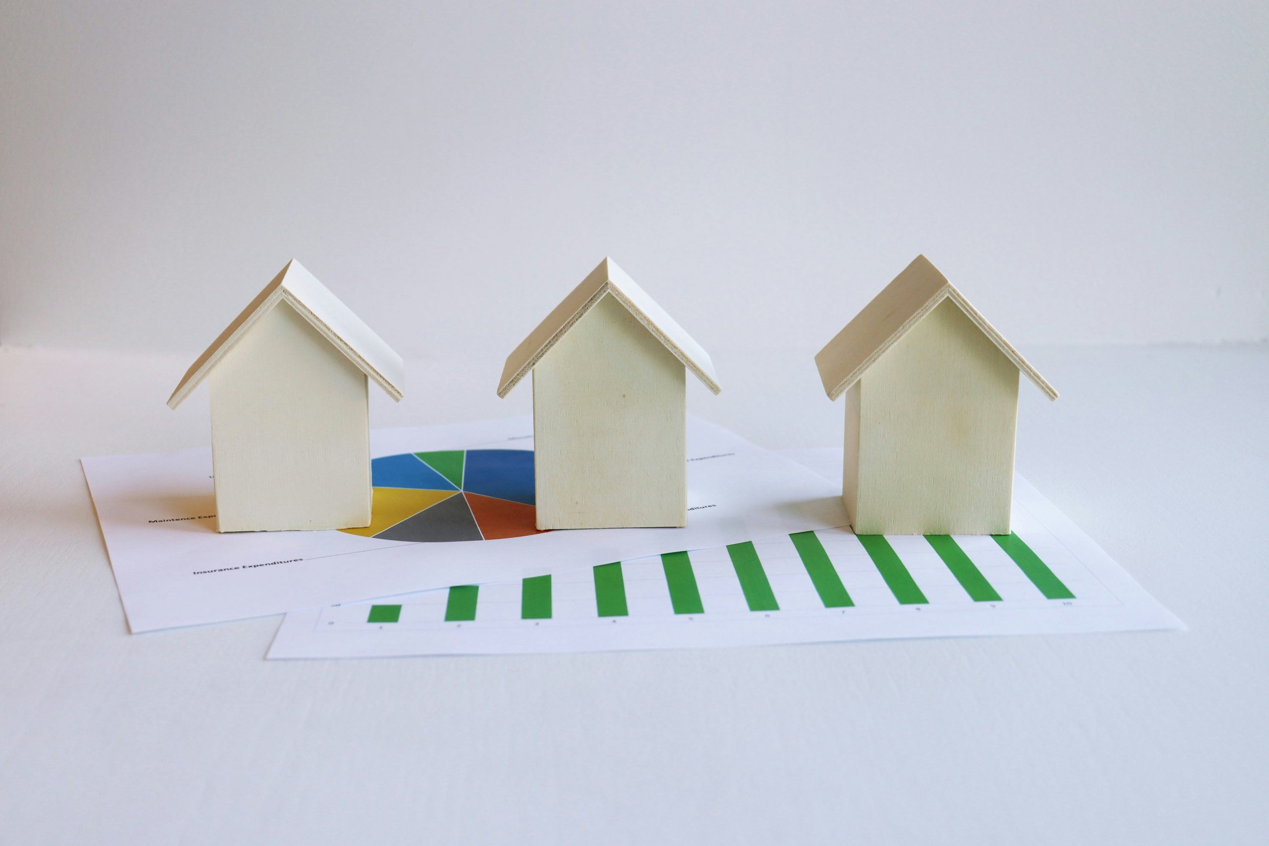 Tres maquetas en miniatura de casas sobre documentos con c&aacute;lculos hipotecarios.