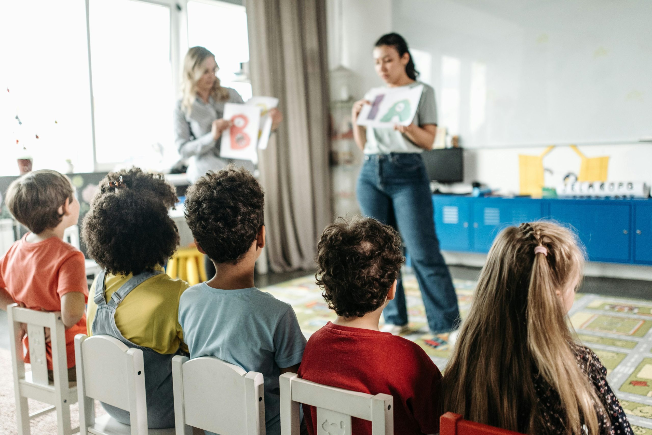 Ni&ntilde;os sentados en sillas blancas dentro de un sal&oacute;n de clases