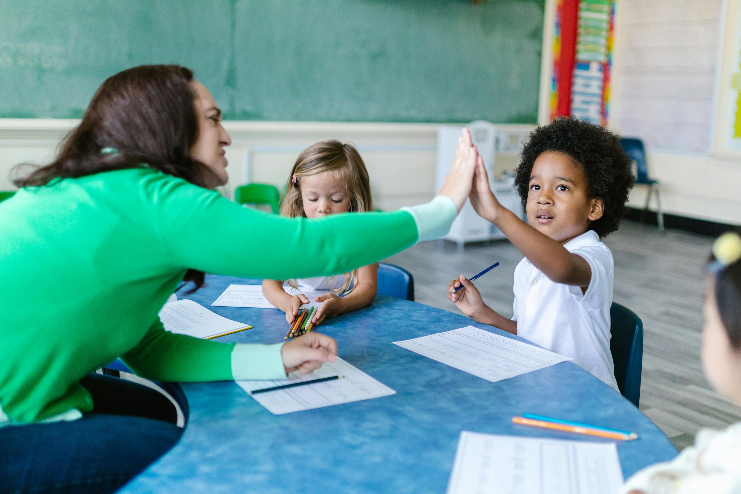 Maestra y ni&ntilde;o d&aacute;ndose la mano en sal&oacute;n de clases.