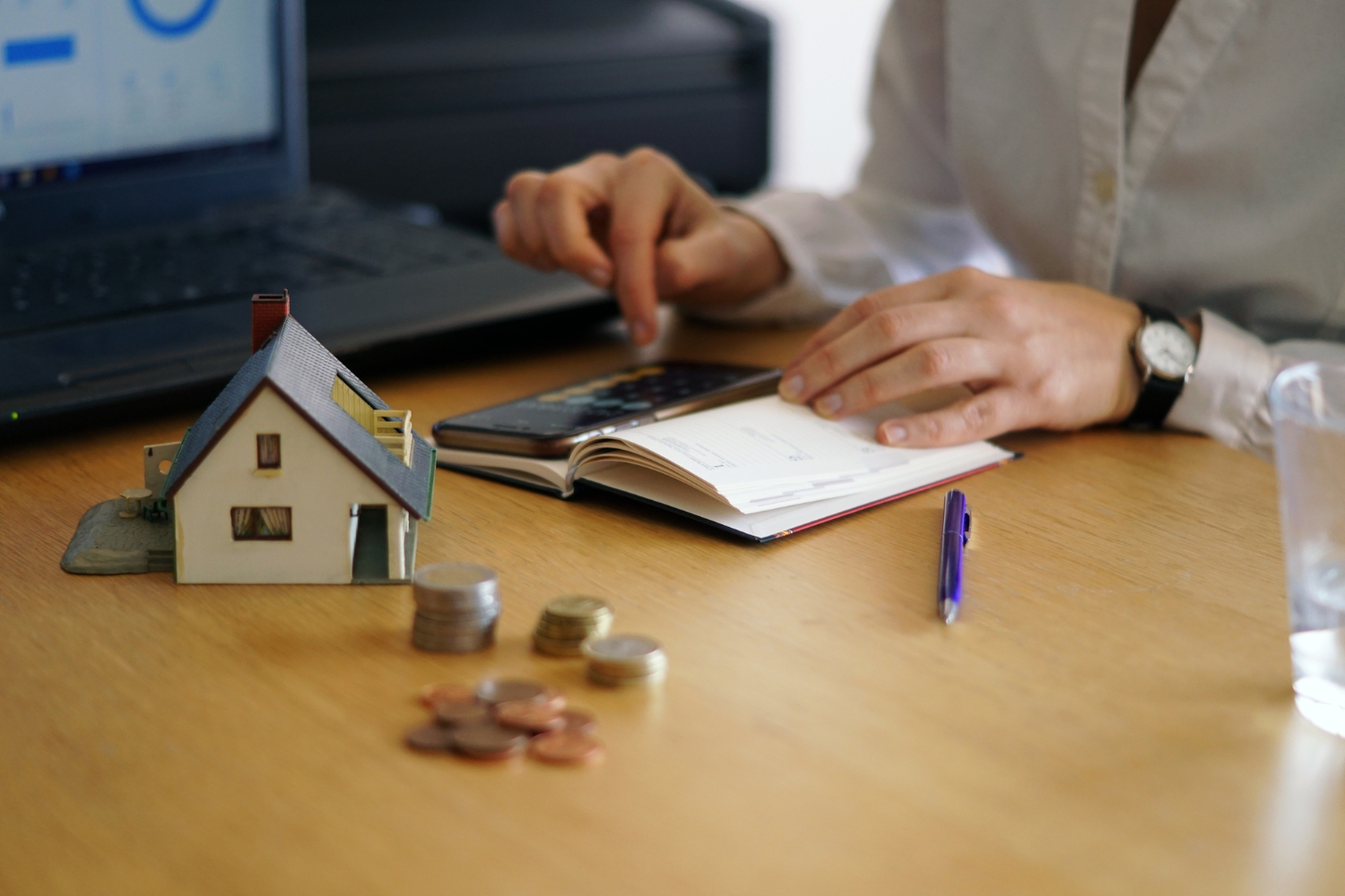 Persona calculando el Impuesto de Bienes Inmuebles en Panam&aacute; con calculadora y modelo de vivienda 